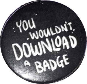 a black round pinbadge with white text that says 'you wouldn't downloa a badge'.